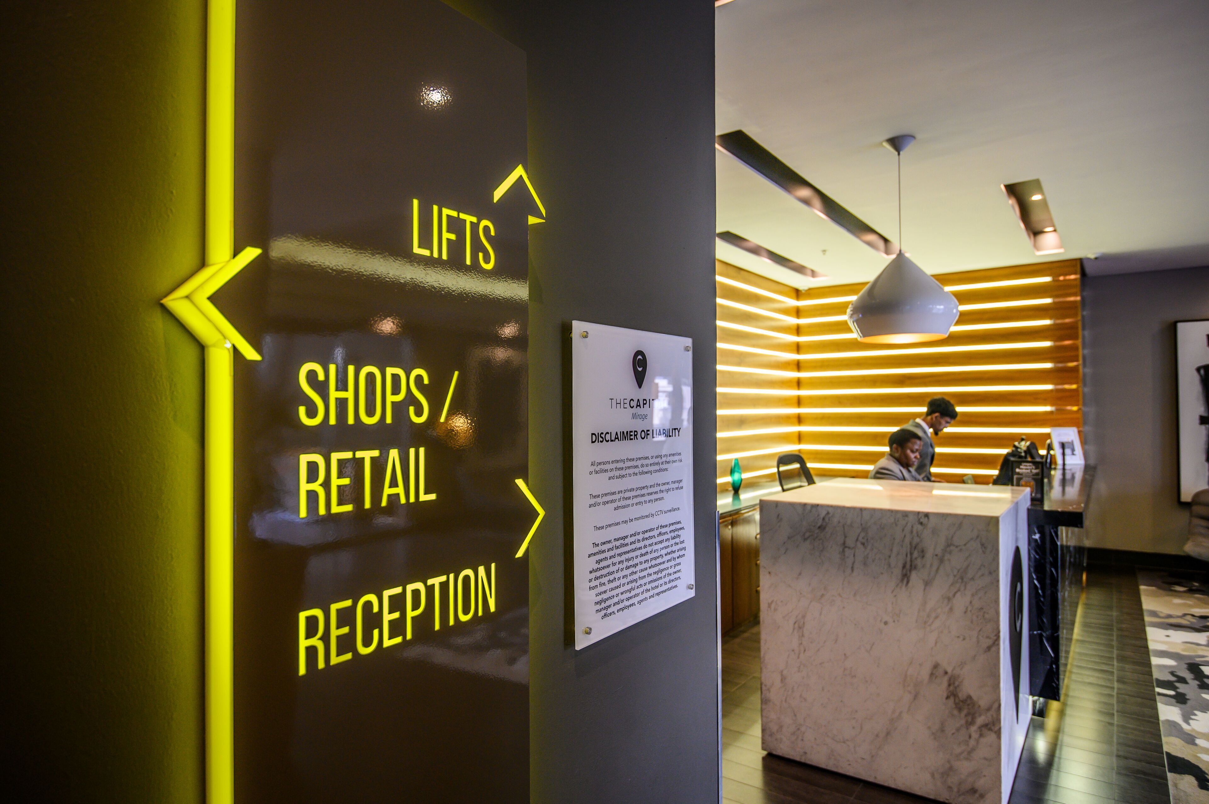 A hotel reception area with a sign indicating directions to lifts, shops, retail, and reception.