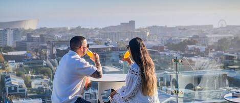 A couple sitting at a table with a city view, overlooking buildings and a Ferris wheel.