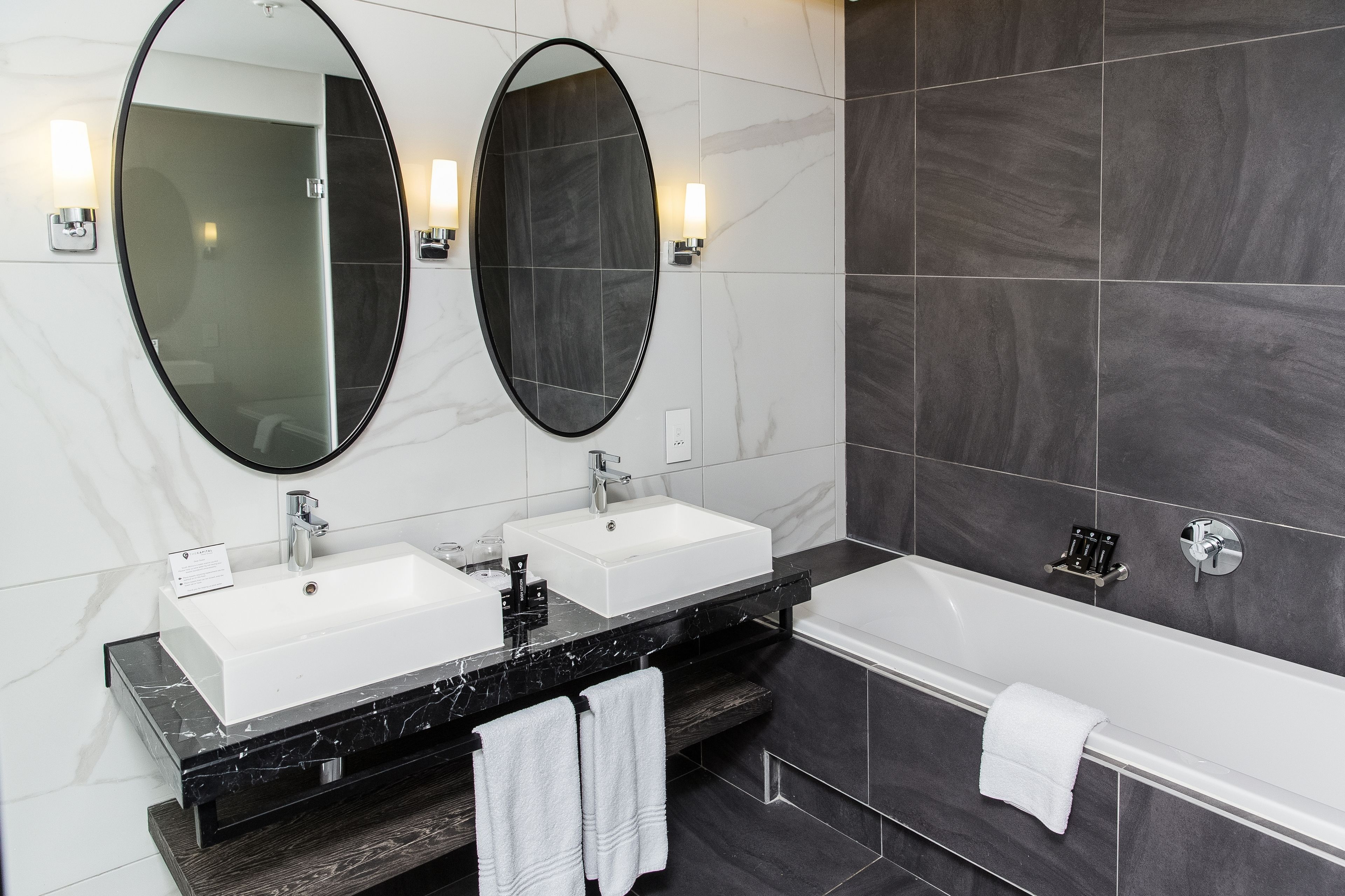 A modern bathroom with two sinks, a large mirror, and a bathtub.