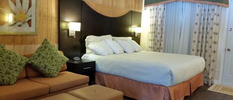 Habitación de hotel con cama, mesita de noche, lámpara, sofá y almohada estampada.