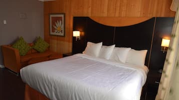 A hotel room with a large bed, a wooden headboard, a sofa with patterned cushions, and two bedside lamps.