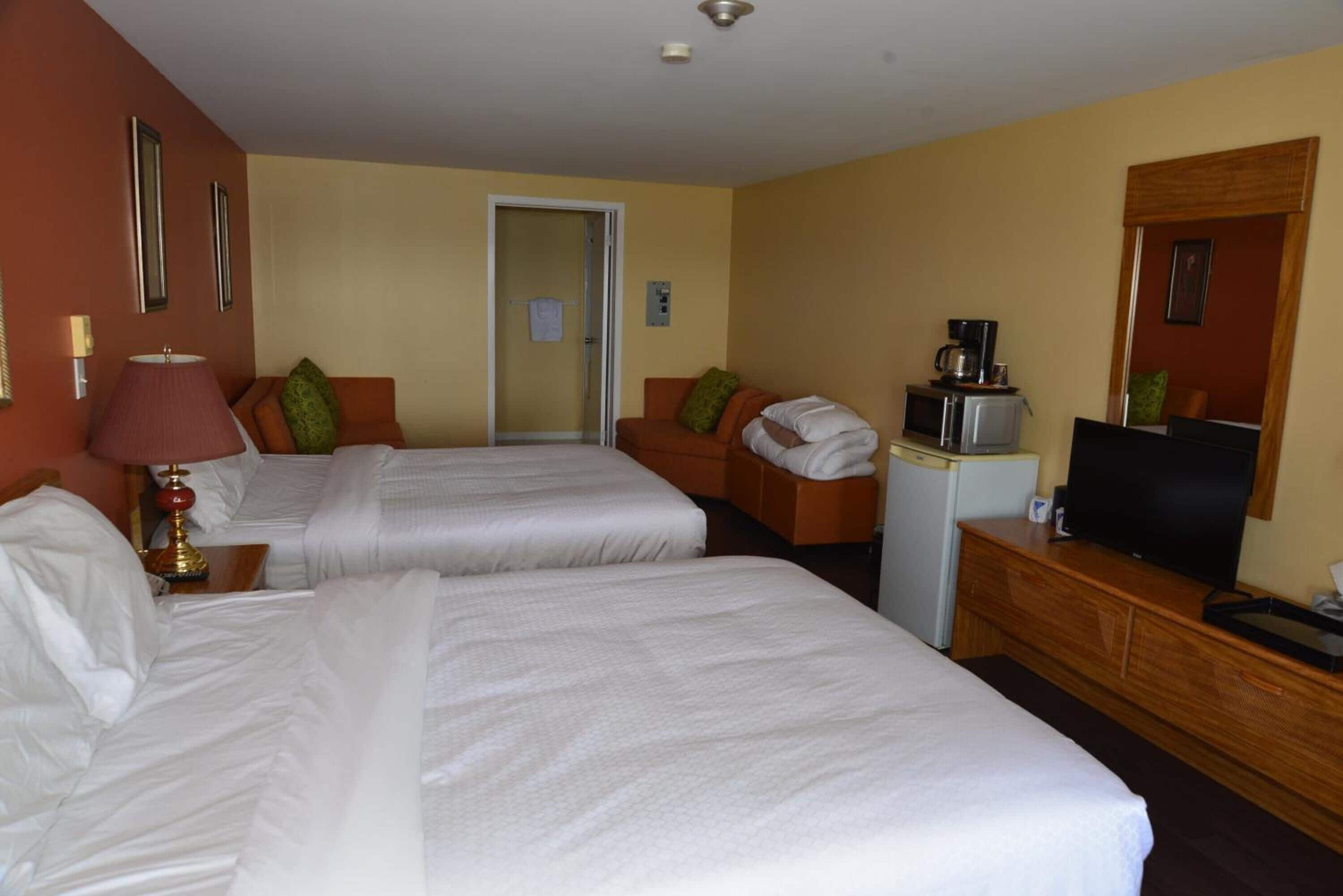 Una habitación de hotel con dos camas, un escritorio, un televisor, una cafetera y un espejo.