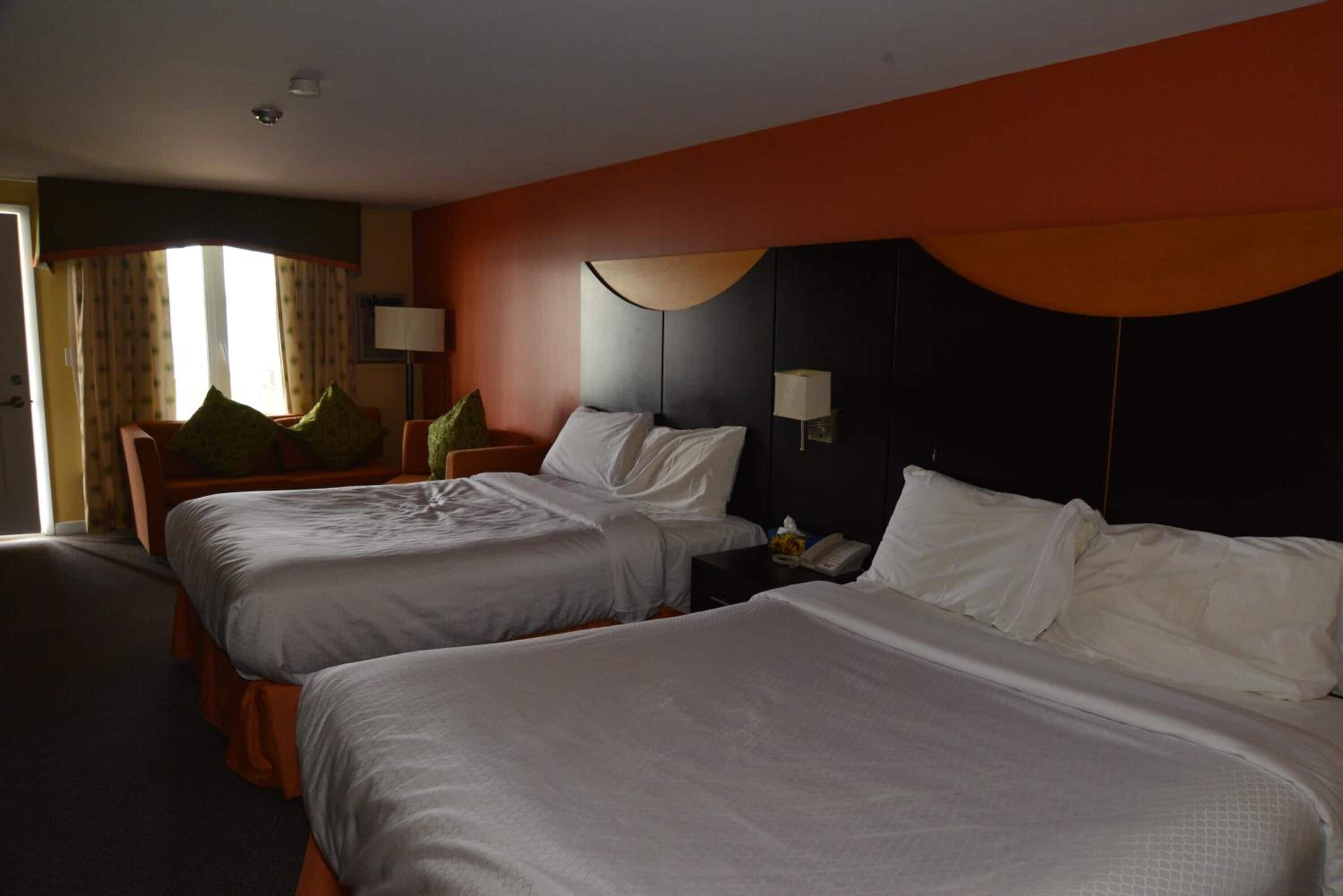 Une chambre d’hôtel avec deux lits, une table de chevet, une lampe et une fenêtre avec des rideaux.