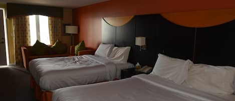 Habitación de hotel con dos camas, una mesita de noche, una lámpara y un ventanal con cortinas.