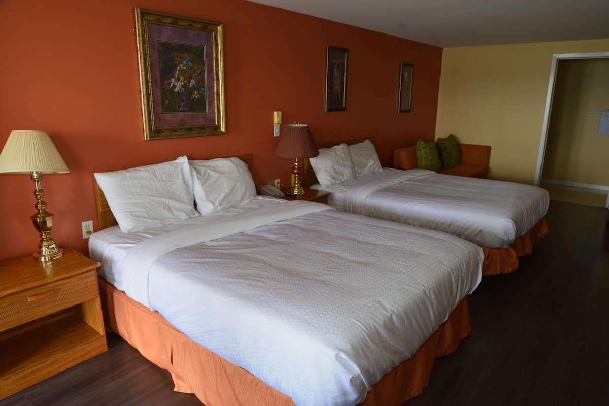 Ein Hotelzimmer mit zwei Betten, einem Nachttisch mit Lampe und einer Tür rechts.