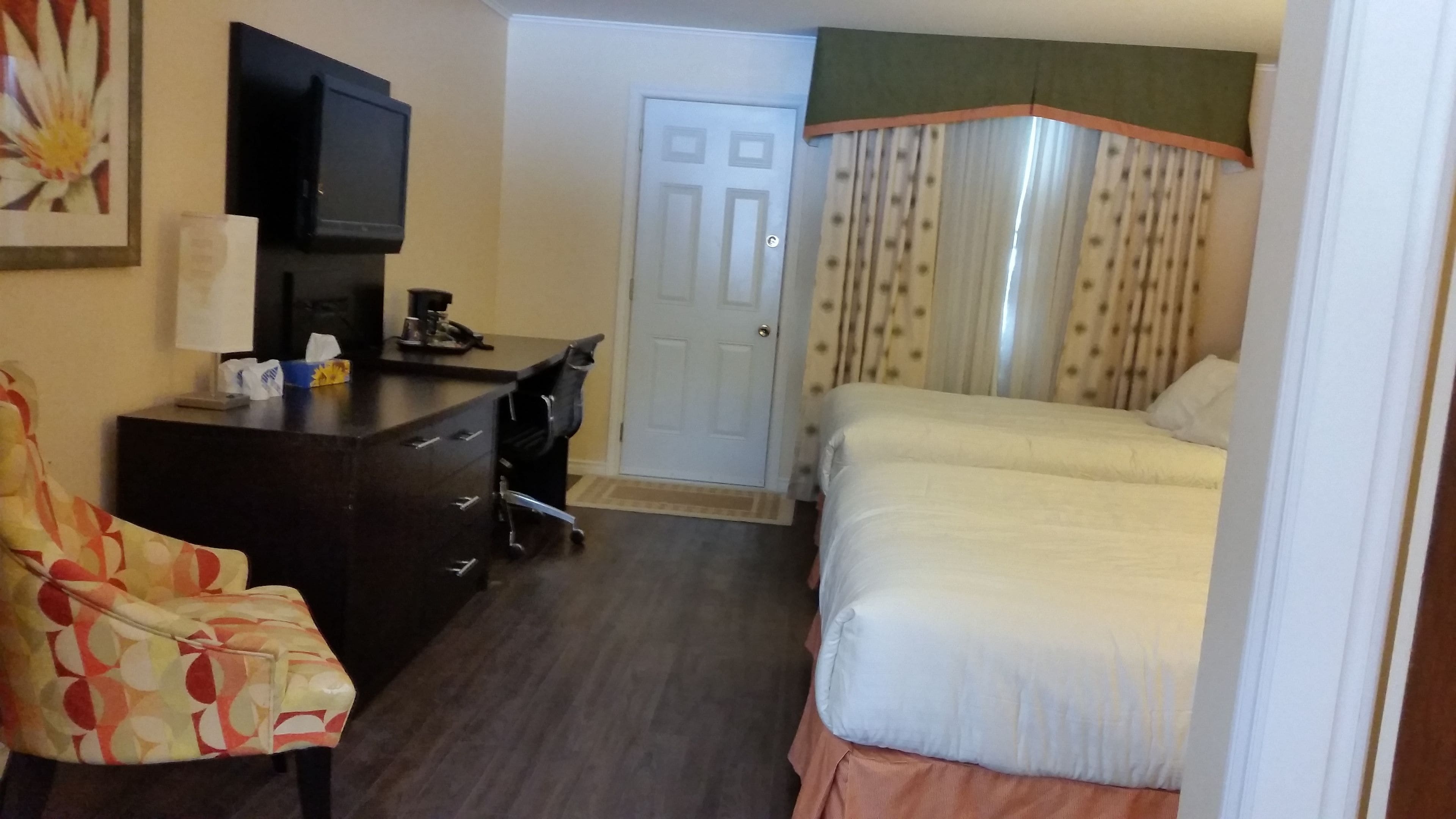 A hotel room with a bed, a desk, a chair, a television, and a door.