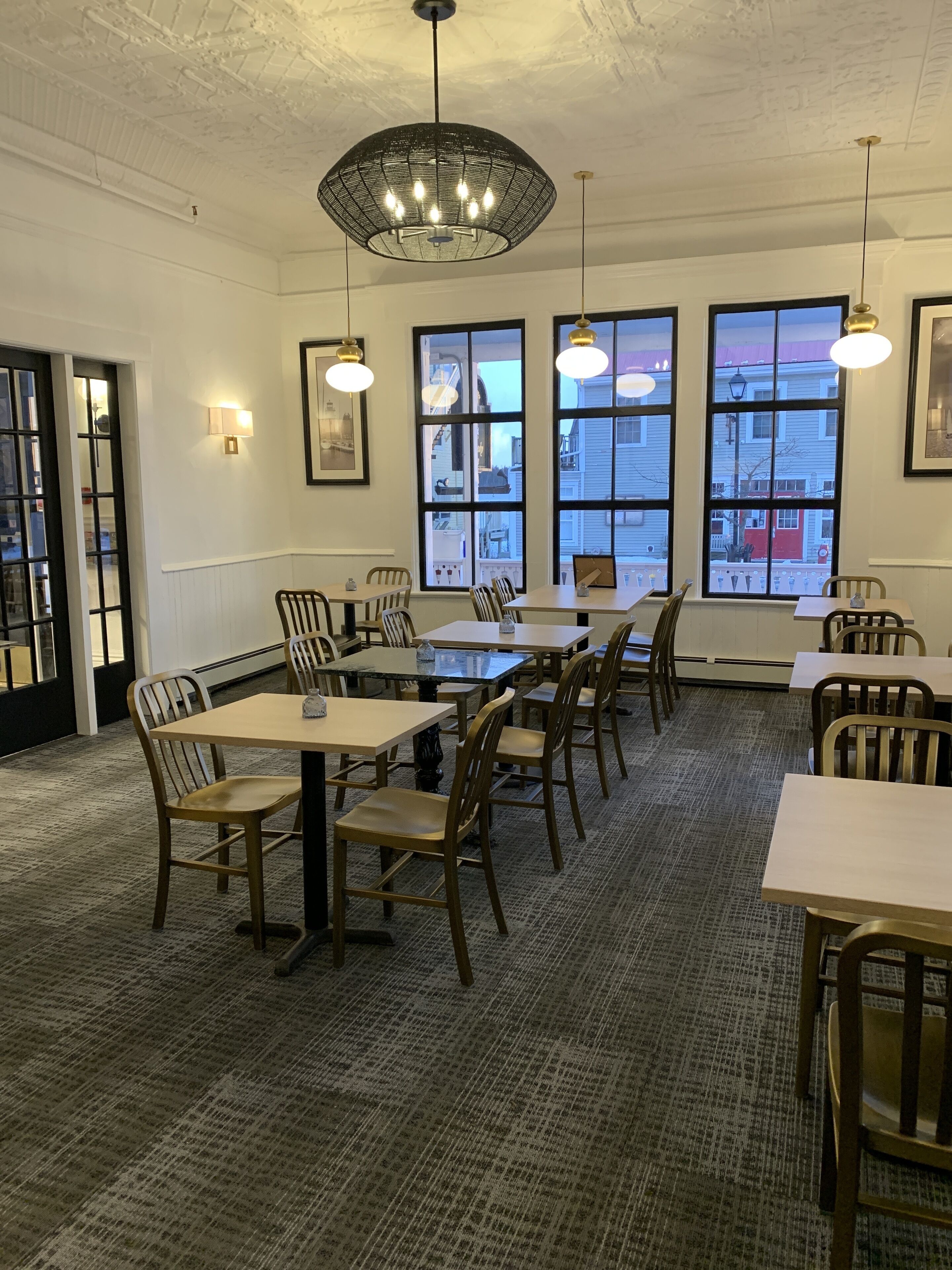 A dining area with tables and chairs, large windows, and hanging pendant lights.