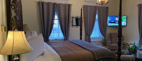 A four-poster bed with a brown bedspread, two bedside lamps, and a television on the wall.