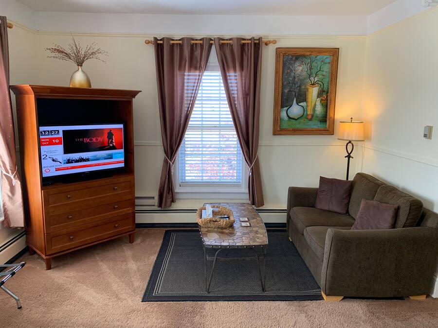 Uma sala de estar com televisão, sofá, mesa de centro, quadro e abajur.