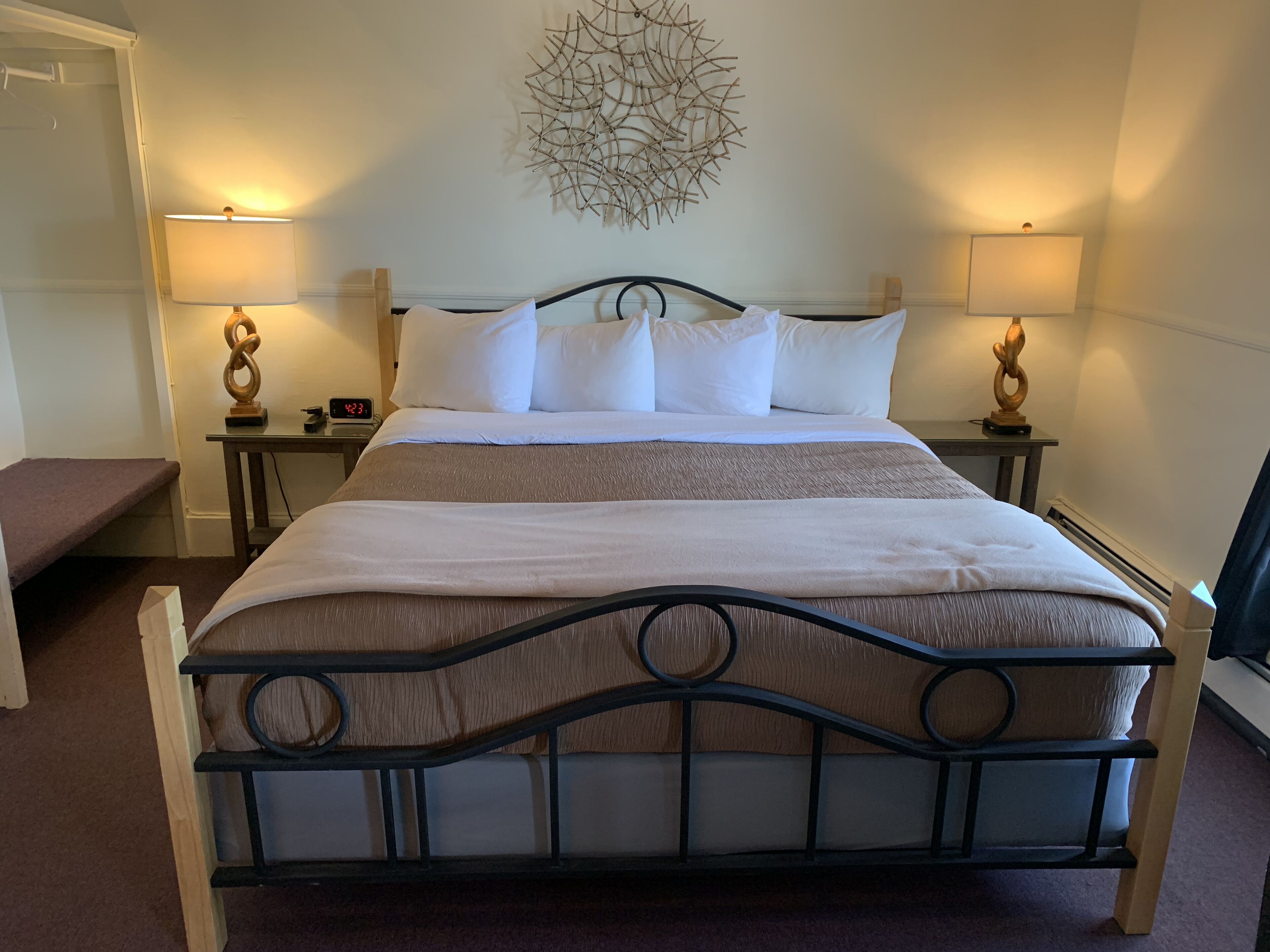 A neatly made bed with a headboard, two bedside tables with lamps, a wall clock, and a decorative wall piece.