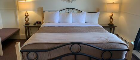 A neatly made bed with a headboard, two bedside tables with lamps, a wall clock, and a decorative wall piece.
