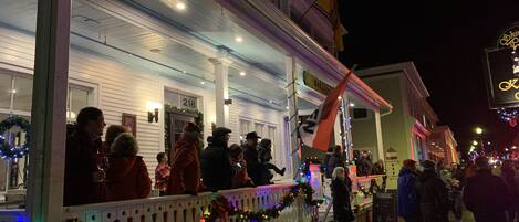 Un edificio con un porche adornado con luces navideñas y guirnaldas, un letrero que dice "Kennedy" y una bandera.