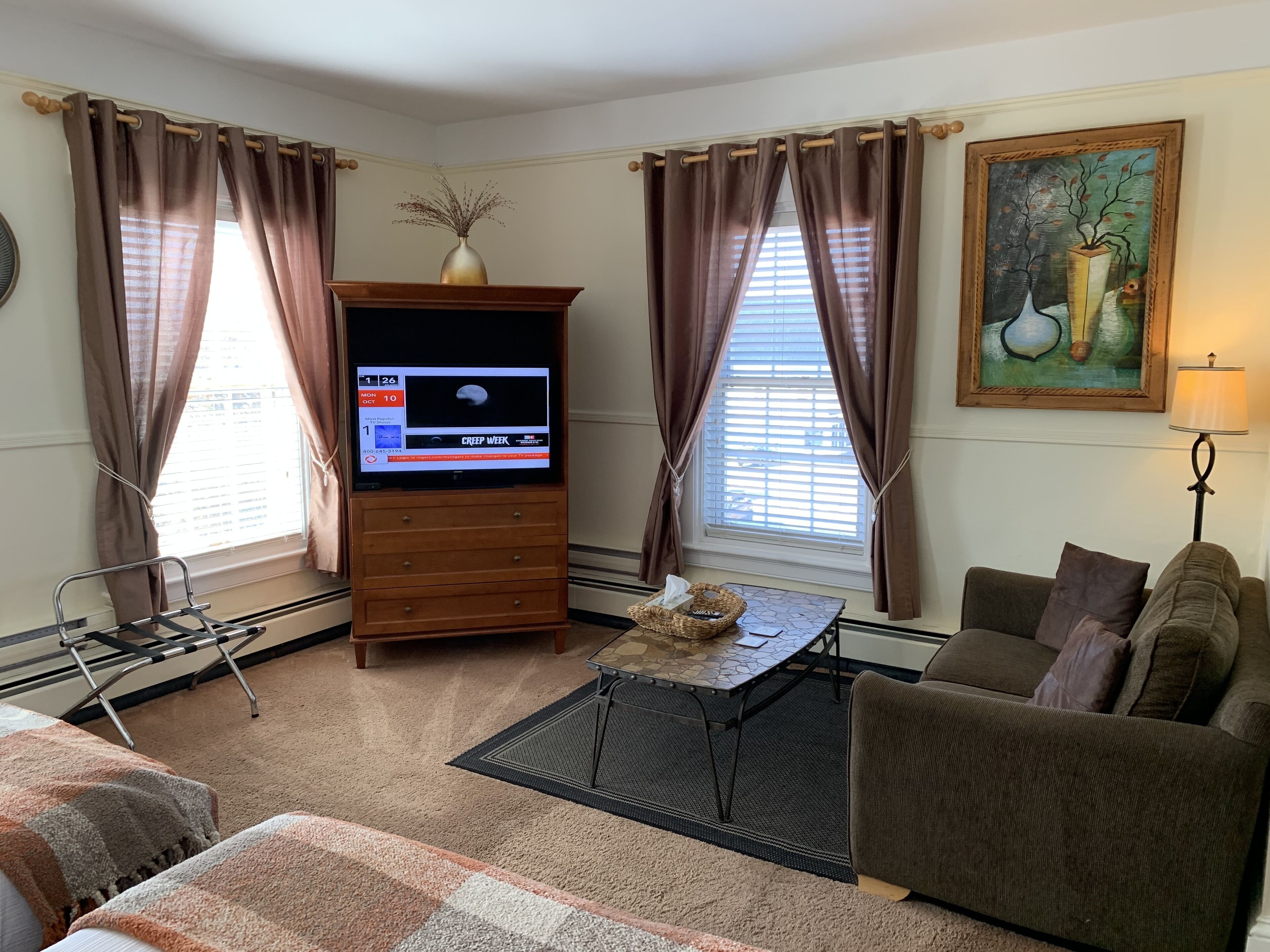 A living room with a flat-screen TV, a sofa, a coffee table, and a painting on the wall.