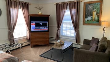 Ein Wohnzimmer mit Flachbildfernseher, einer Couch, einem Couchtisch und einem Gemälde an der Wand.