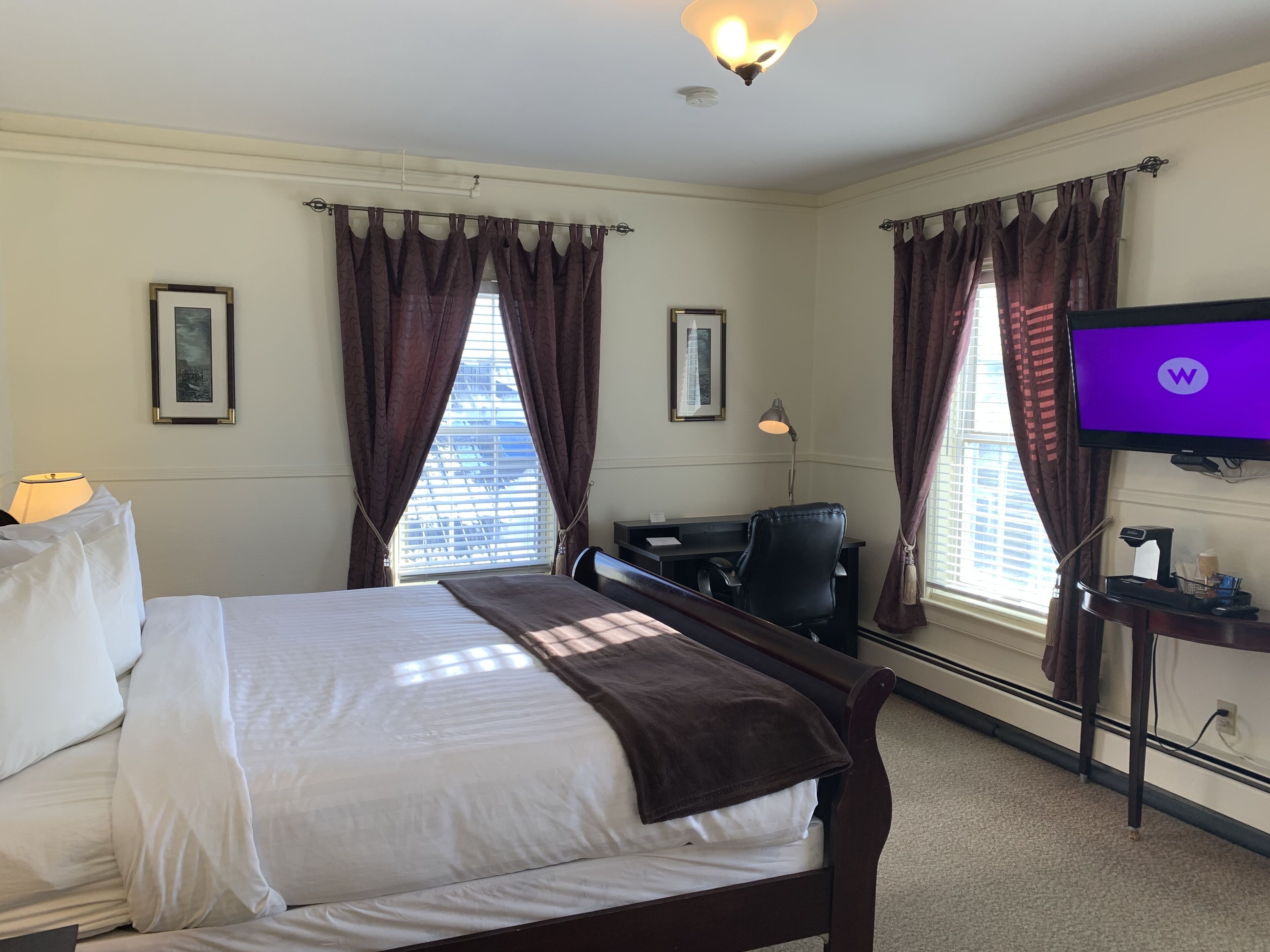 Une chambre d’hôtel équipée d’un lit, d’un bureau, d’une chaise, d’une télévision et de fenêtres avec des rideaux.