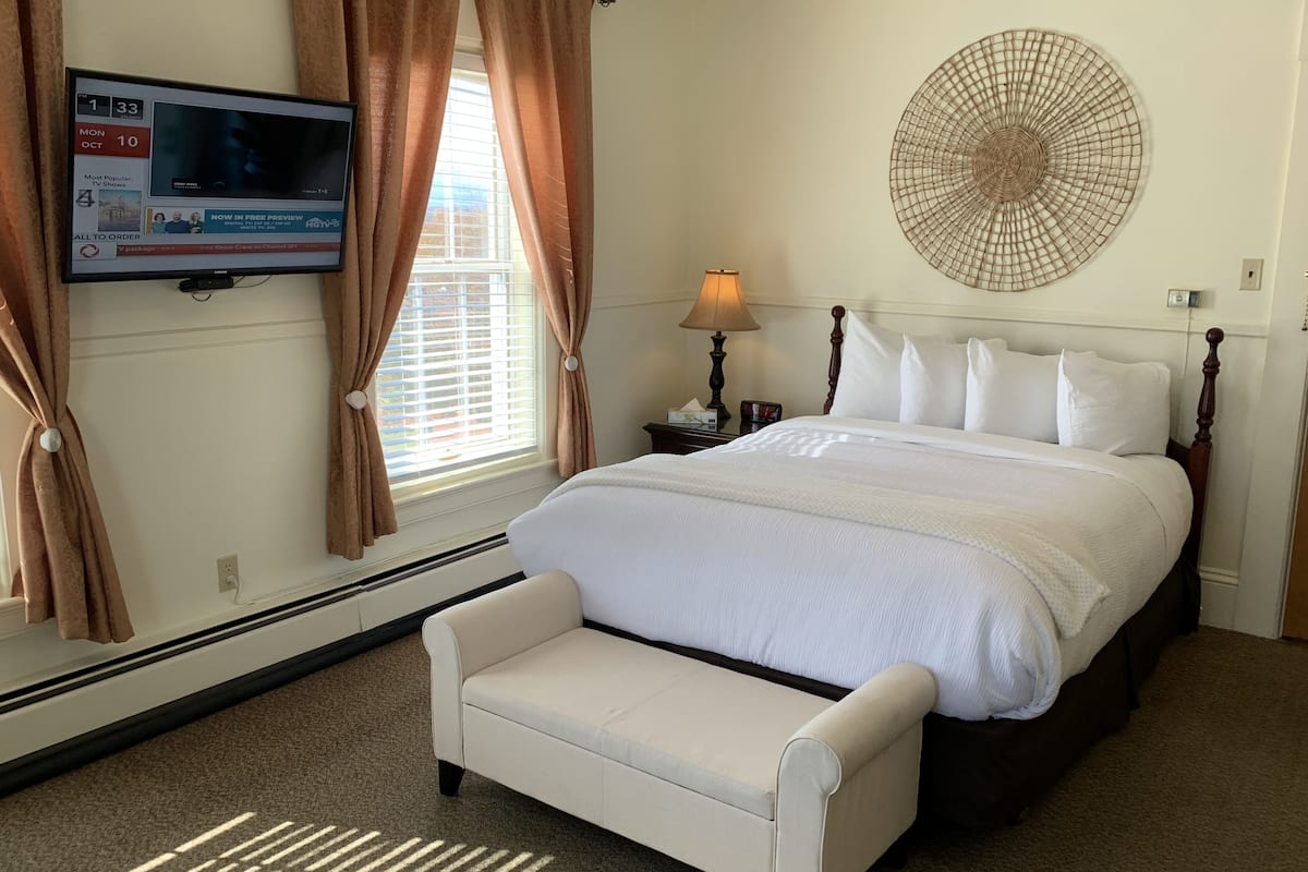 Habitación de hotel con cama, televisor montado en la pared, mesita de noche con lámpara y un gran adorno mural.
