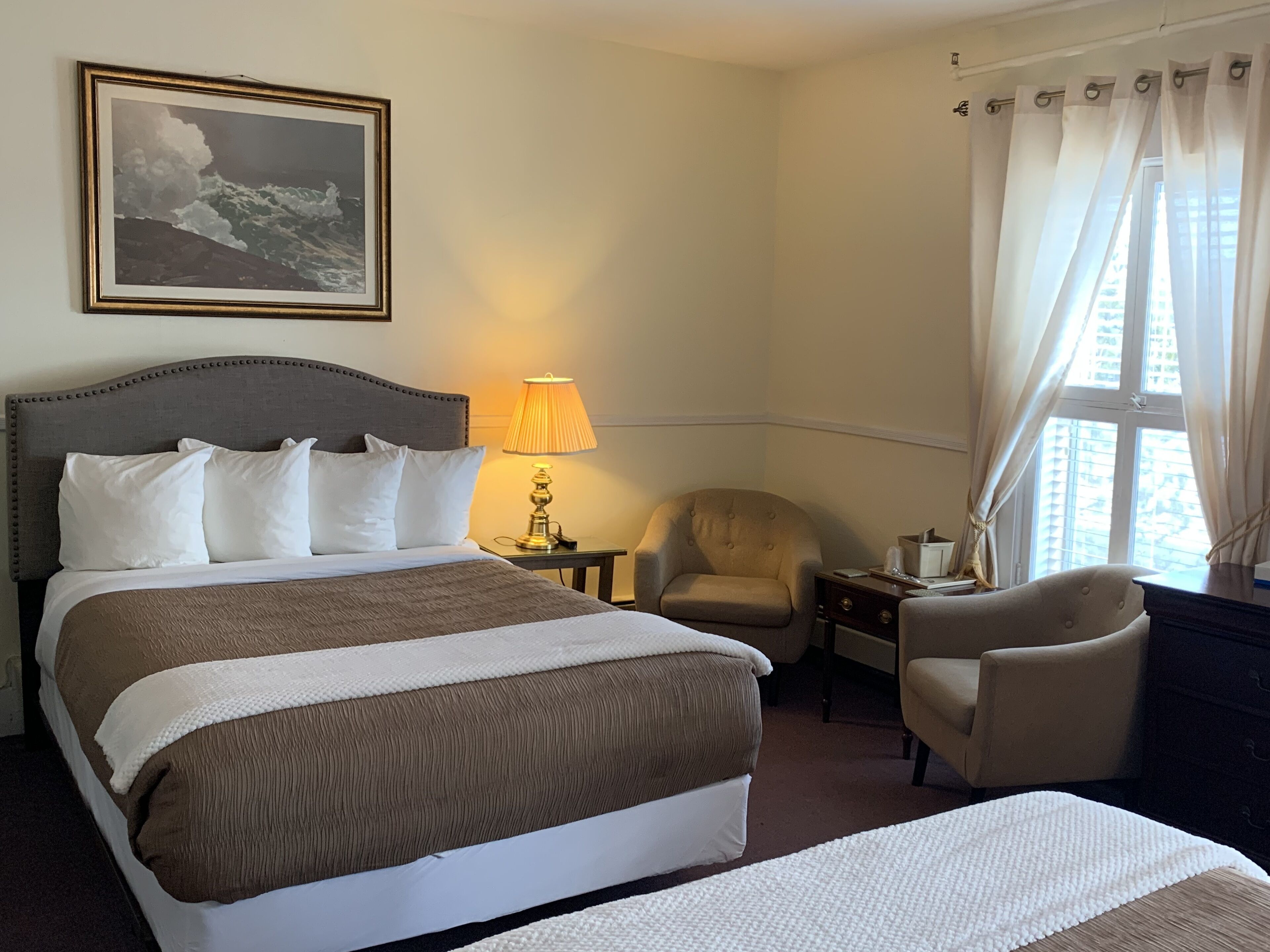 Une chambre d’hôtel avec un grand lit, une chaise, une lampe et une fenêtre avec des rideaux.
