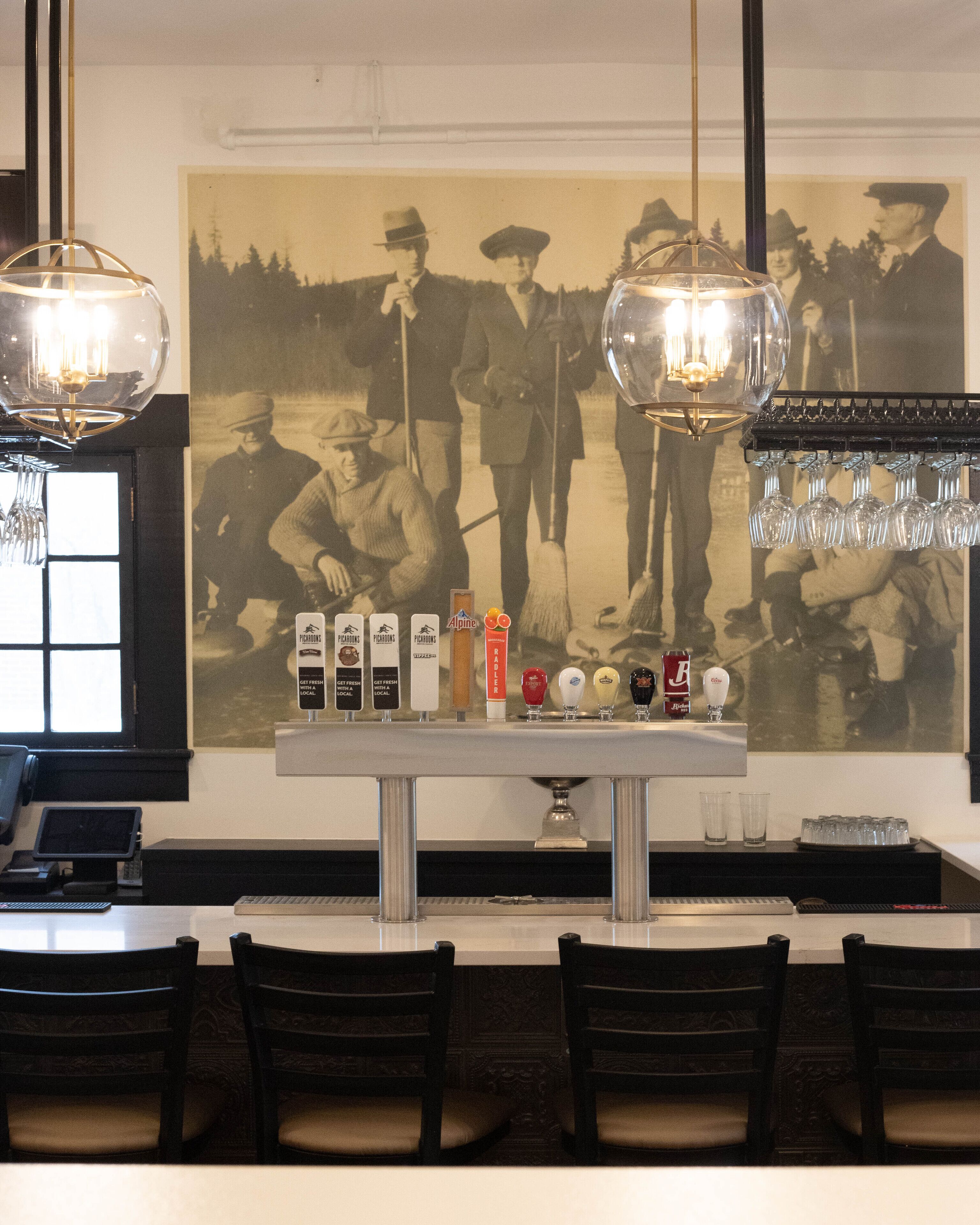 Un rincón de bar con una fotografía antigua en la pared, varias opciones de cerveza en grifo y una lámpara moderna.