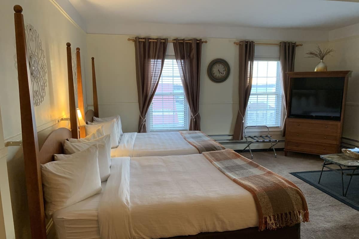 Una habitación de hotel con dos camas, televisión, reloj y ventana con cortinas.
