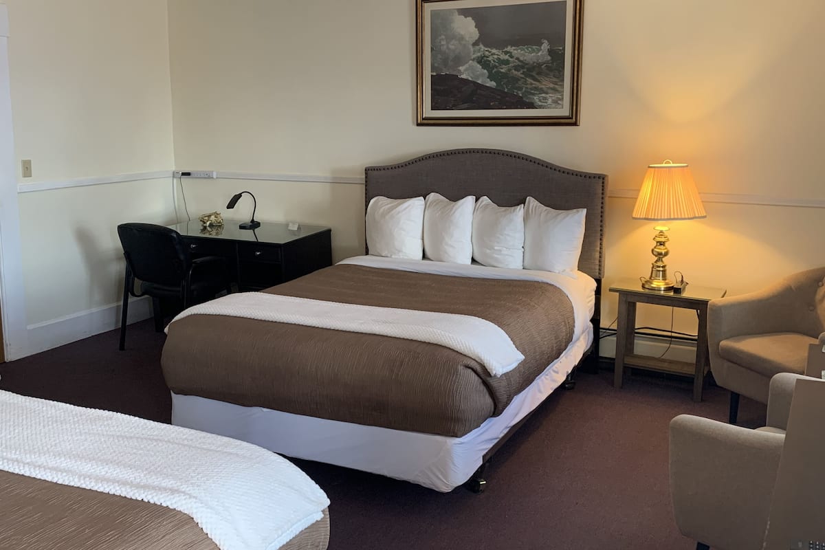 Habitación de hotel con una cama grande, un escritorio con silla, una lámpara y un cuadro en la pared.