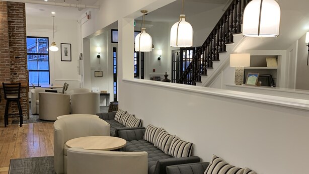 A modern living room with a sectional sofa, round tables, and a staircase with a black railing. - Kennedy House (St. Andrews)