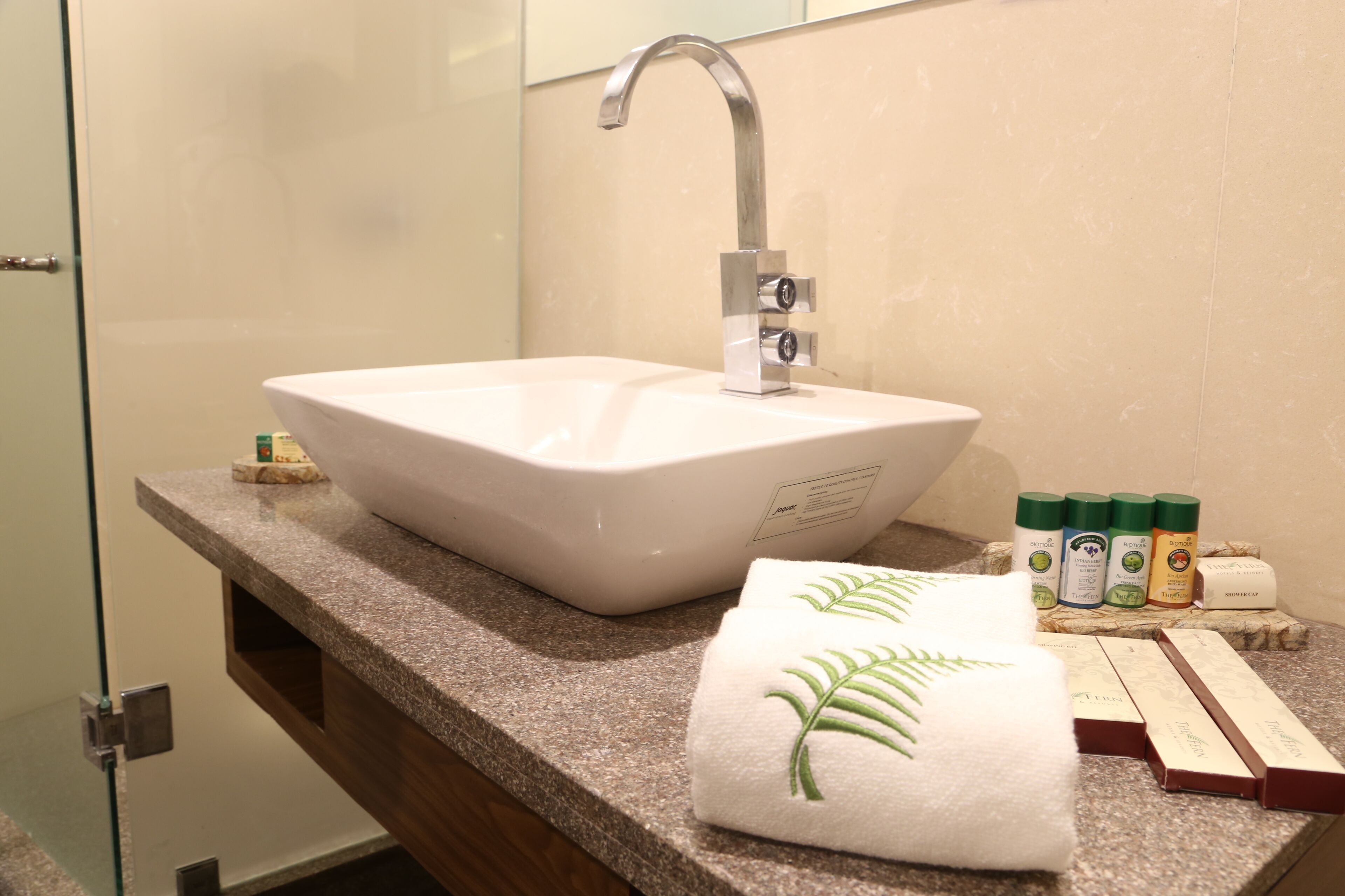 Un baño con un lavamanos blanco, un grifo moderno, una toalla con diseño de hoja verde y un juego de artículos de aseo sobre la encimera.