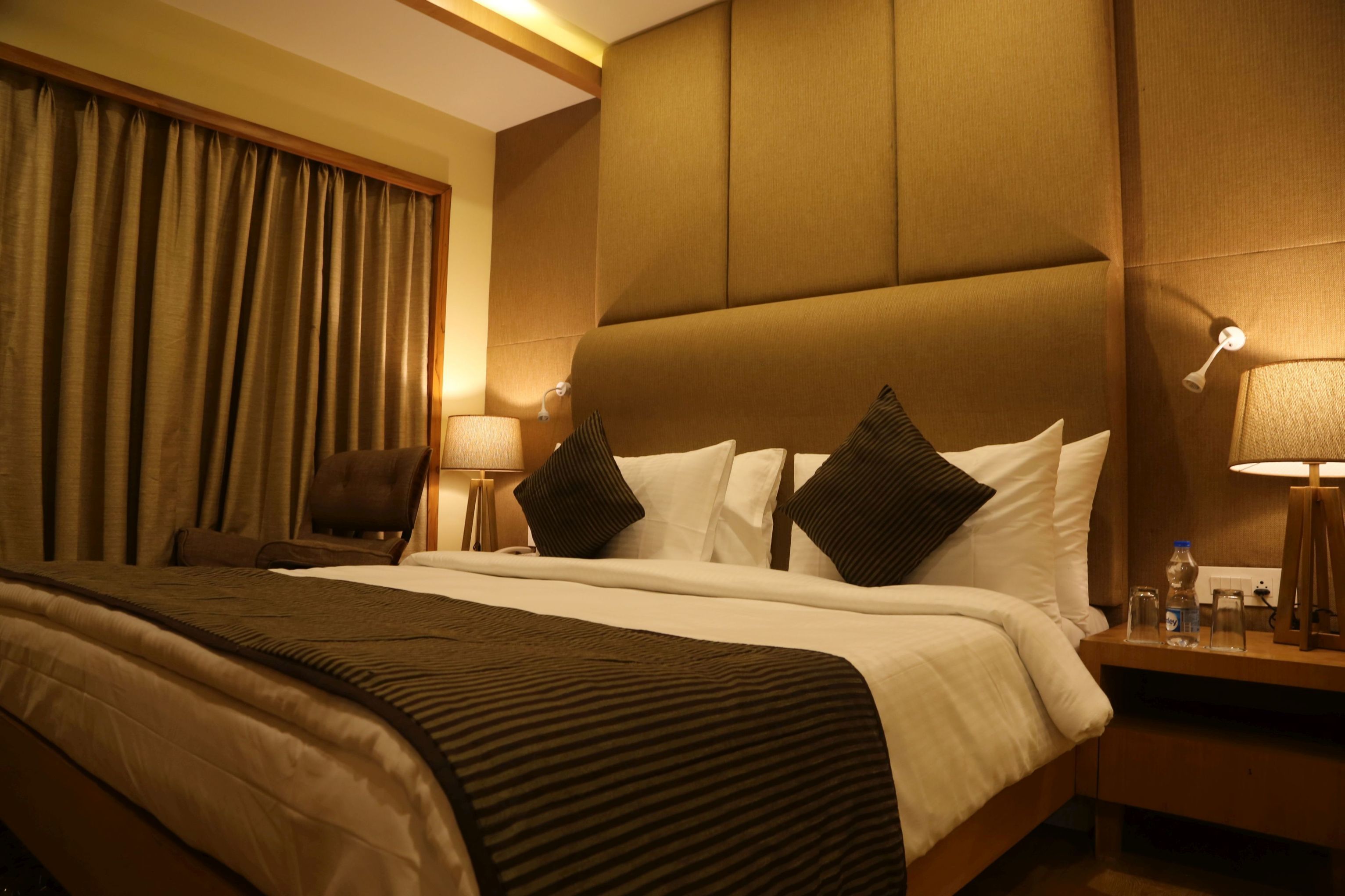 A hotel room with a large bed, a wooden headboard, a nightstand with a lamp, and a chair.