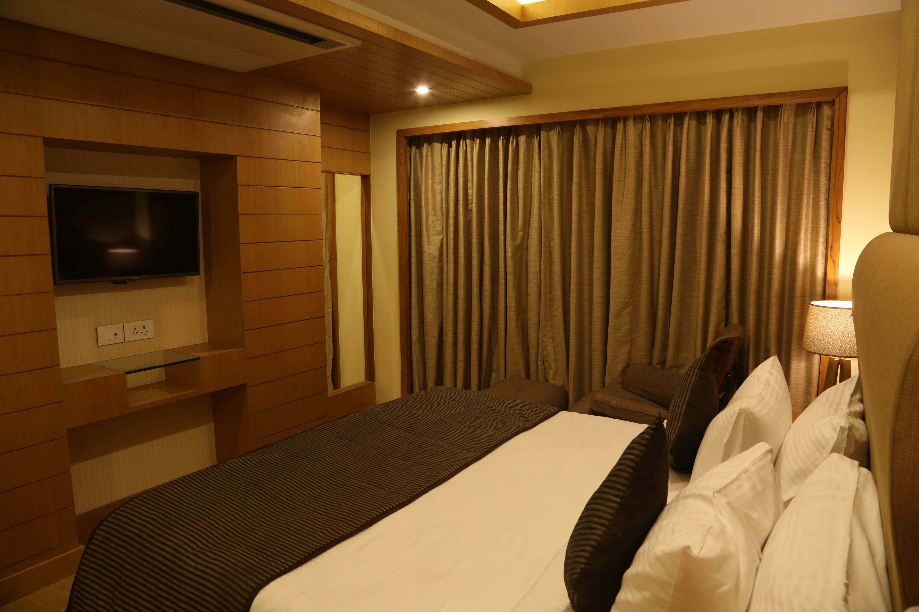 Une chambre d’hôtel dotée d’un grand lit, d’un téléviseur à écran plat fixé au mur, d’un bureau avec une lampe et d’une fenêtre avec des rideaux.