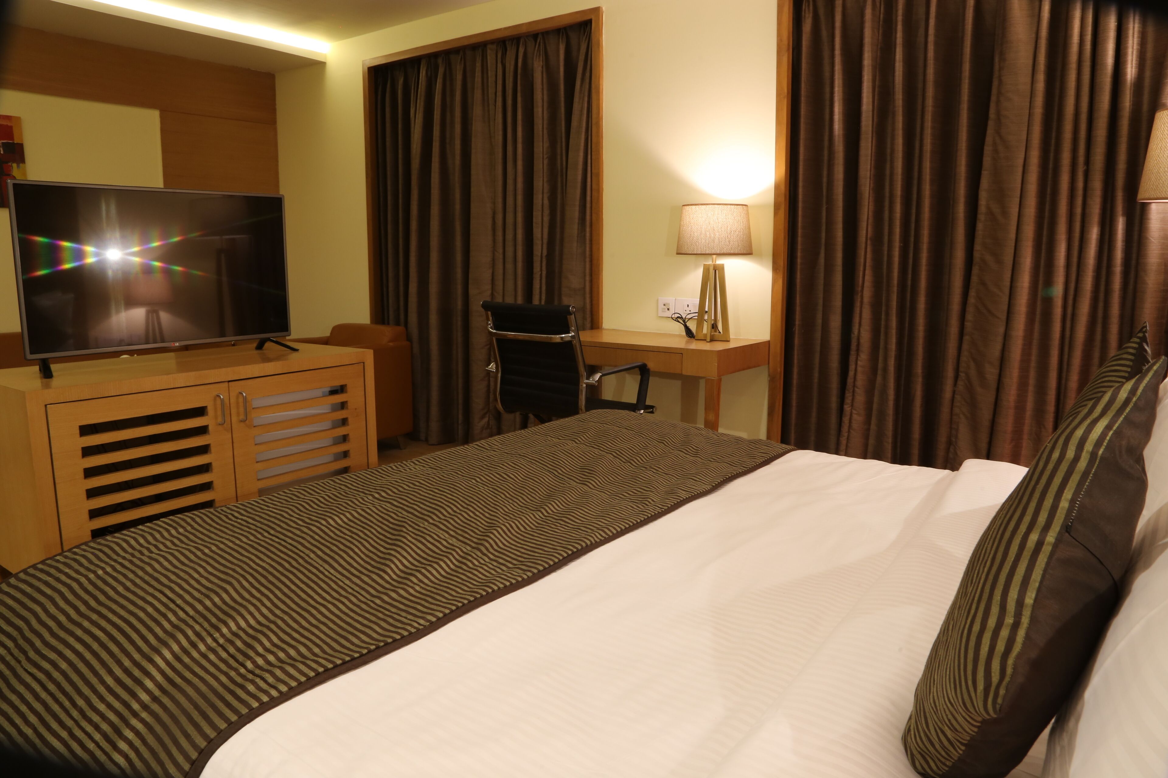 A hotel room with a bed, a desk, a chair, a television, and curtains.