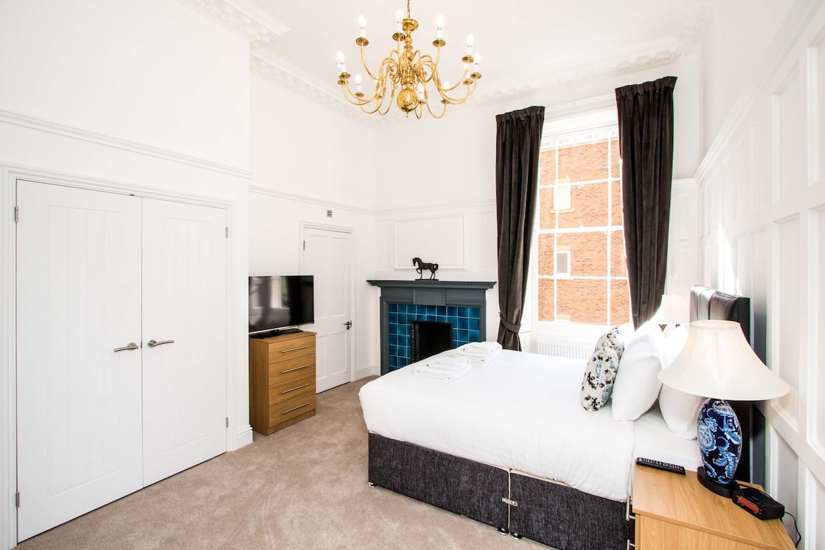 A hotel room with a large bed, a television, a fireplace, and a chandelier.