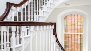 Una imponente escalera con balaustres blancos y barandillas de madera oscura, que conduce a un ventanal con vidrieras de colores.