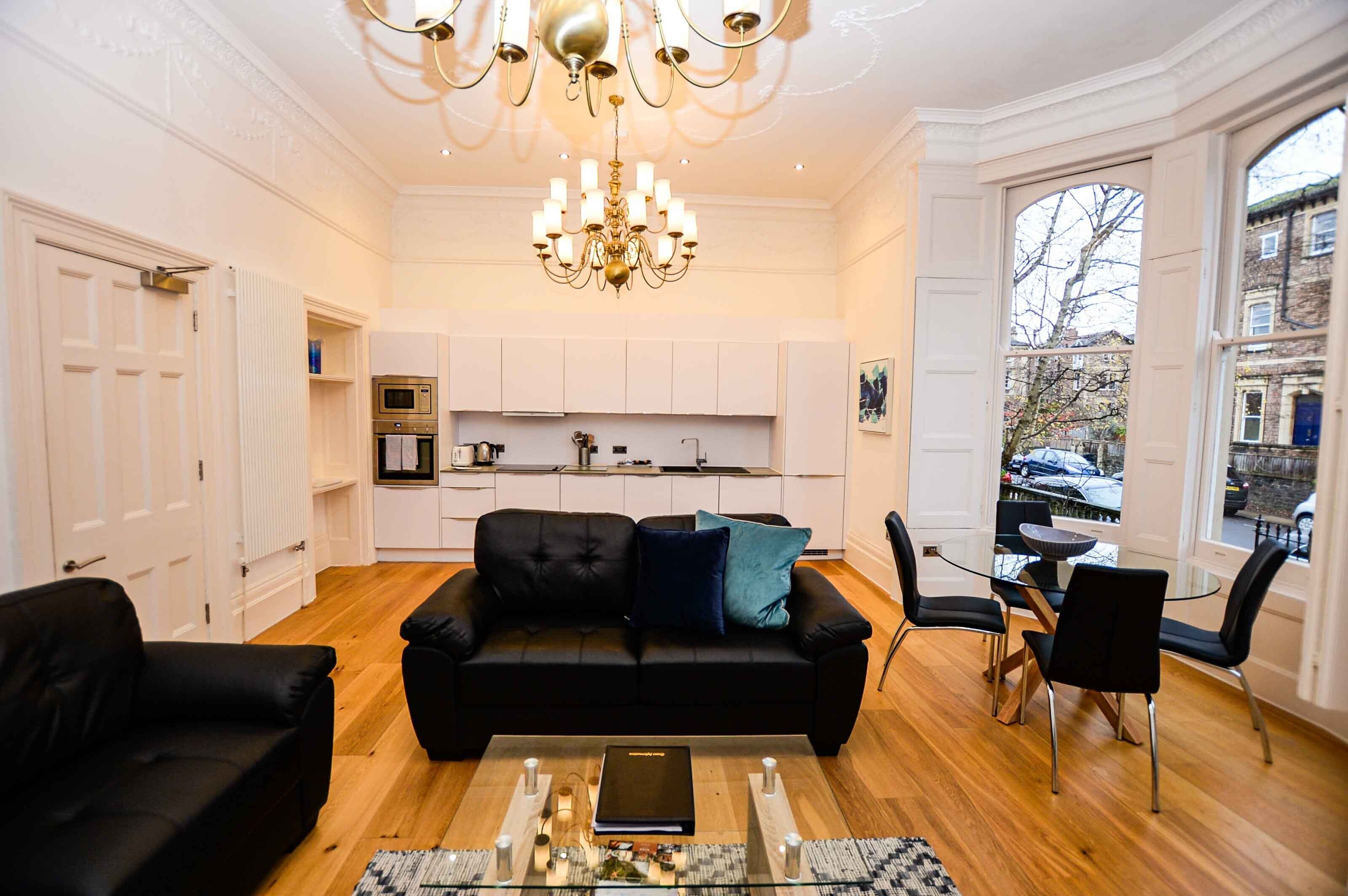 Un salon moderne avec un canapé en cuir noir, une table basse en verre et un coin repas comprenant une table en verre et des chaises noires.
