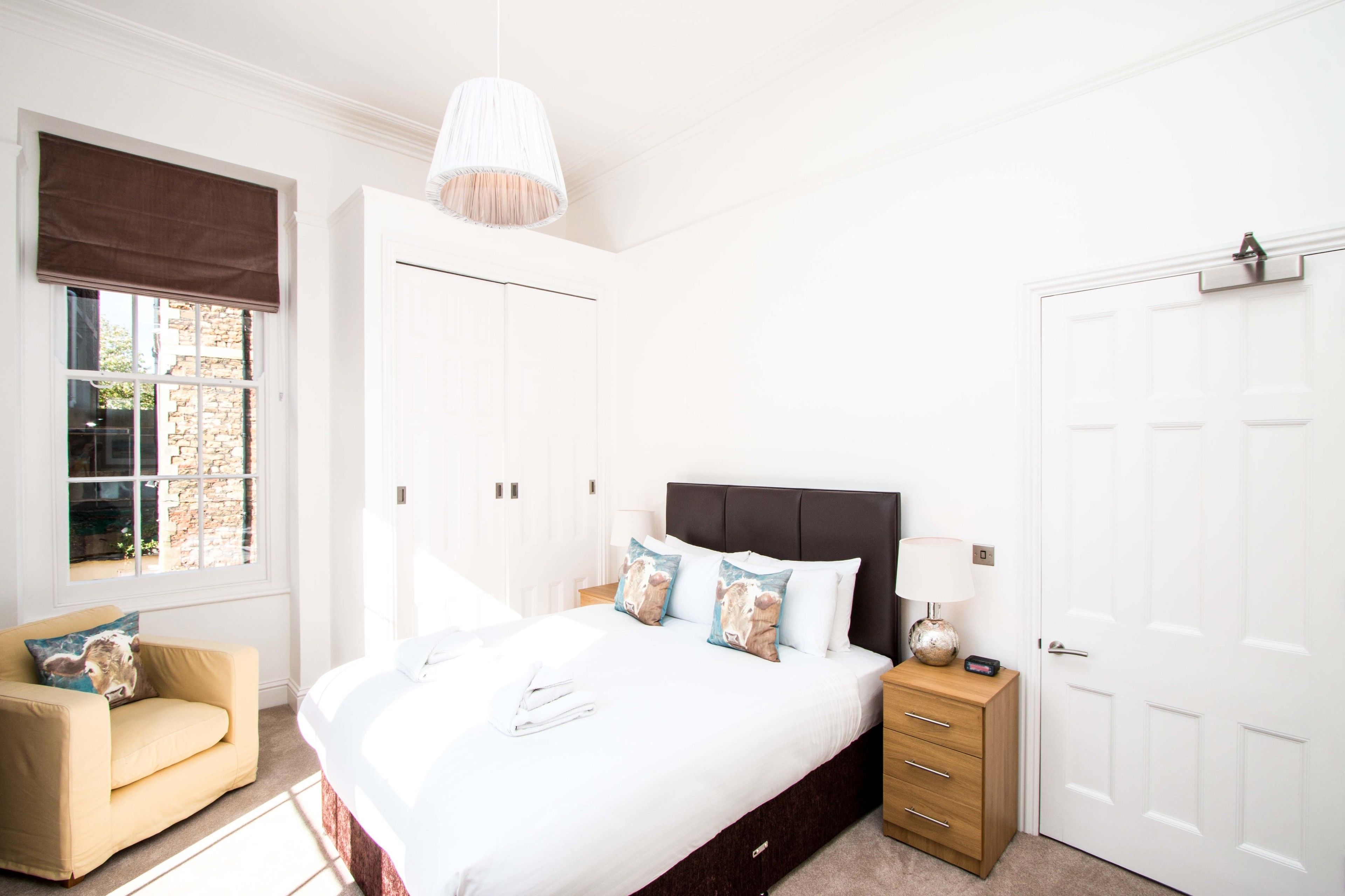 Een slaapkamer met een groot bed, nachtkastjes, een garderobe, een raam met uitzicht en een hanglamp.