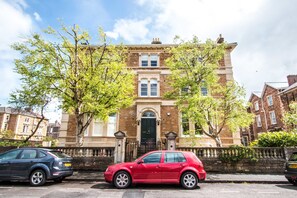 A two-story brick building with a black door and windows, parked cars in front, and trees with green leaves. - Your Stay Bristol Beaufort House (Bristol)
