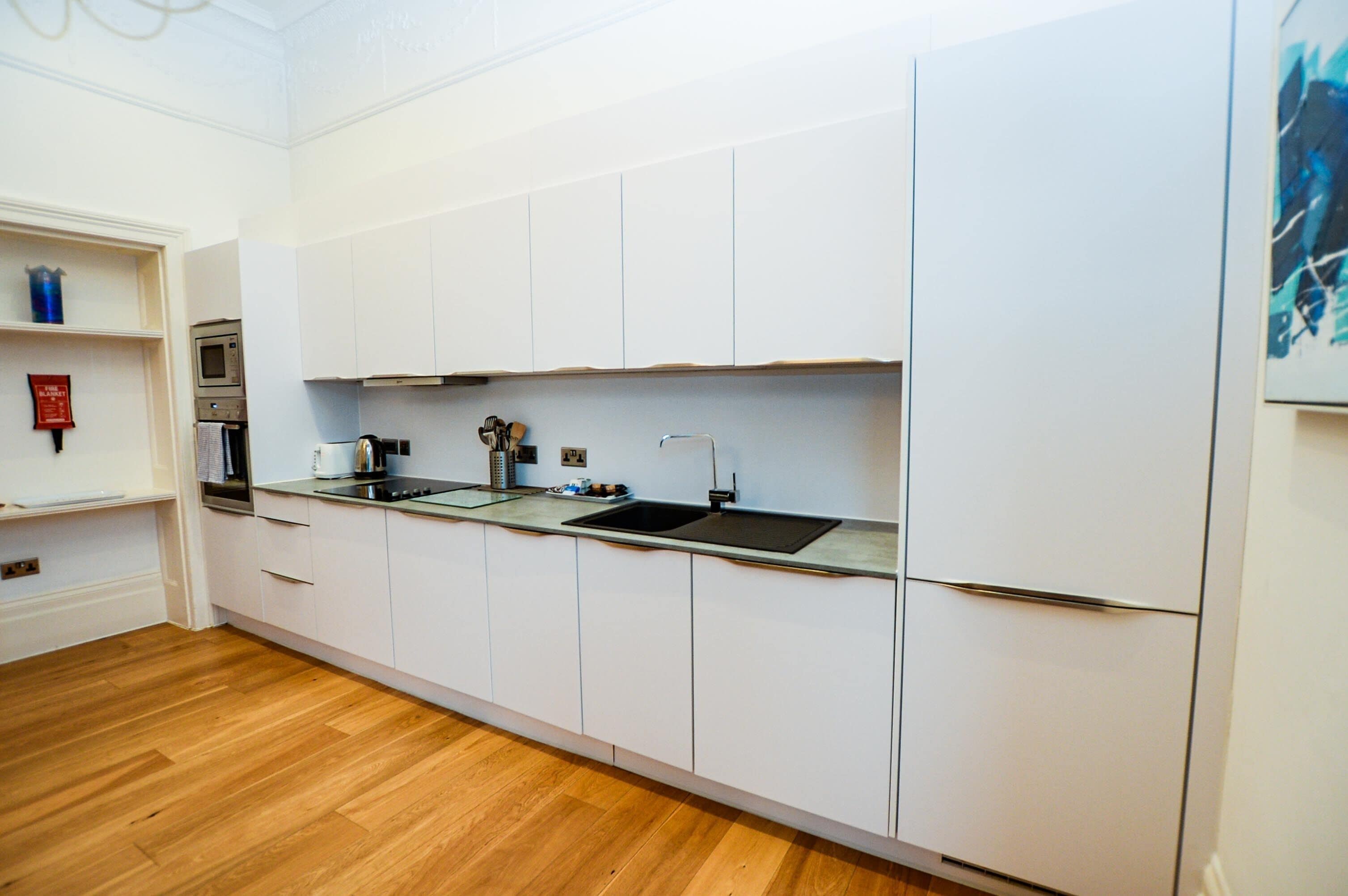 Een moderne keuken met witte kasten, een roestvrijstalen spoelbak en een ingebouwde oven.
