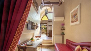 A room with a dining table set for two, a red sofa, a staircase leading to an upper level, and a wall-mounted air conditioner. - B&B La Casa nel Giardino (Piano di Sorrento)
