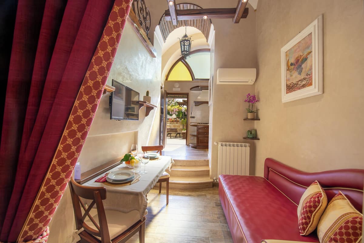 Une pièce comprenant une table à manger dressée pour deux personnes, un canapé rouge, un escalier menant à l’étage supérieur et un climatiseur fixé au mur.