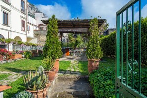 A courtyard with a pergola, potted plants, and a stone pathway leading to a building entrance.