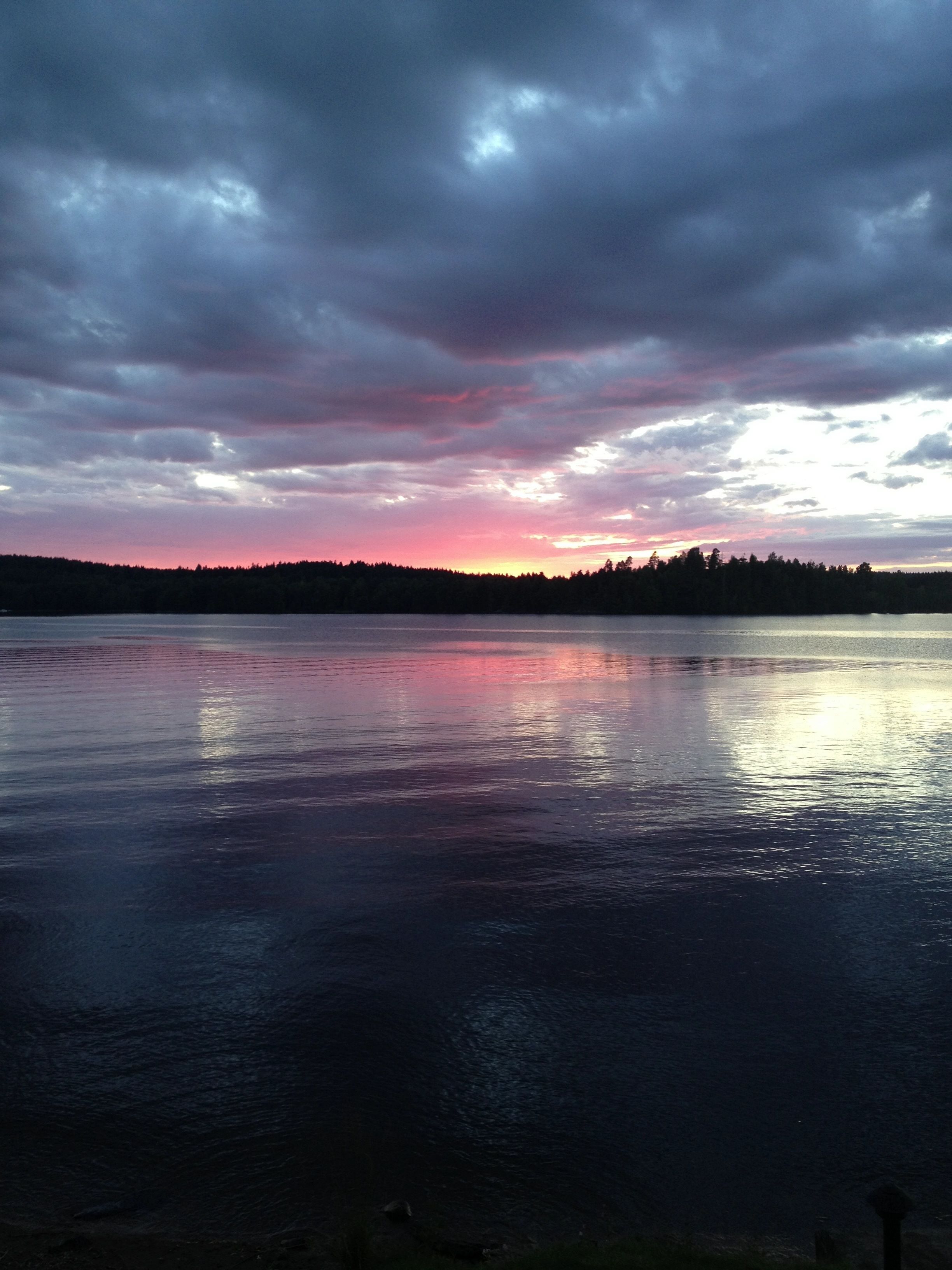 A calm lake at sunset with a forested shoreline.