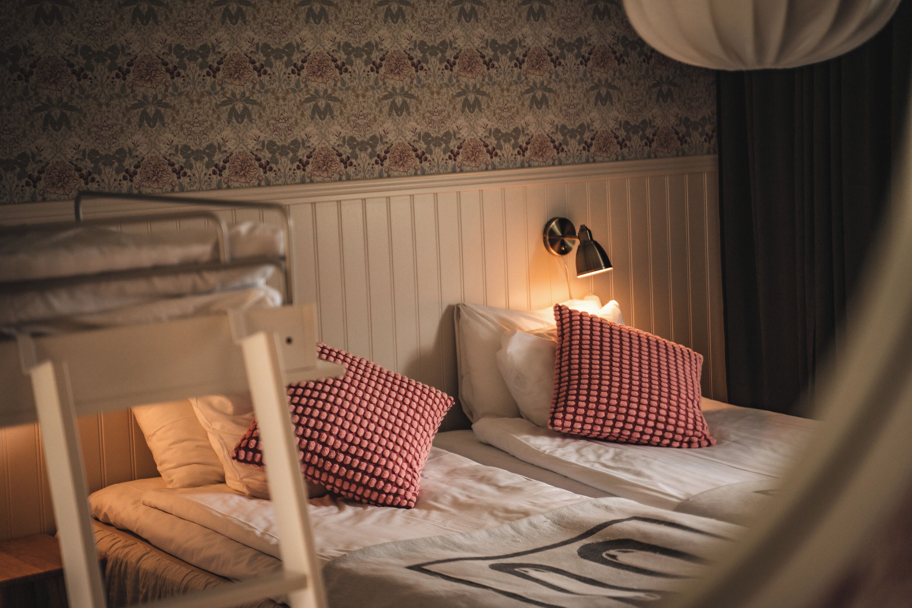 Een stapelbed met twee kussens, een aan de muur bevestigde lamp en behang met een patroon.