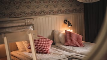 Een stapelbed met twee kussens, een aan de muur bevestigde lamp en behang met een patroon.