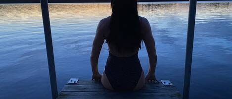 A person sitting on a wooden dock overlooking a calm body of water during sunset.