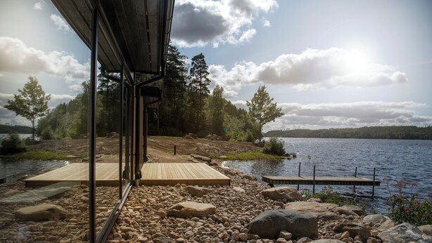 A lakeside cabin with a wooden deck, a dock, and a view of the lake and surrounding trees. - Två Skyttlar (Orby)