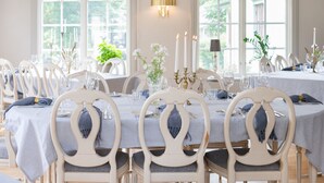 A dining area with white chairs and tables, candles, and a vase with flowers. - Två Skyttlar (Orby)