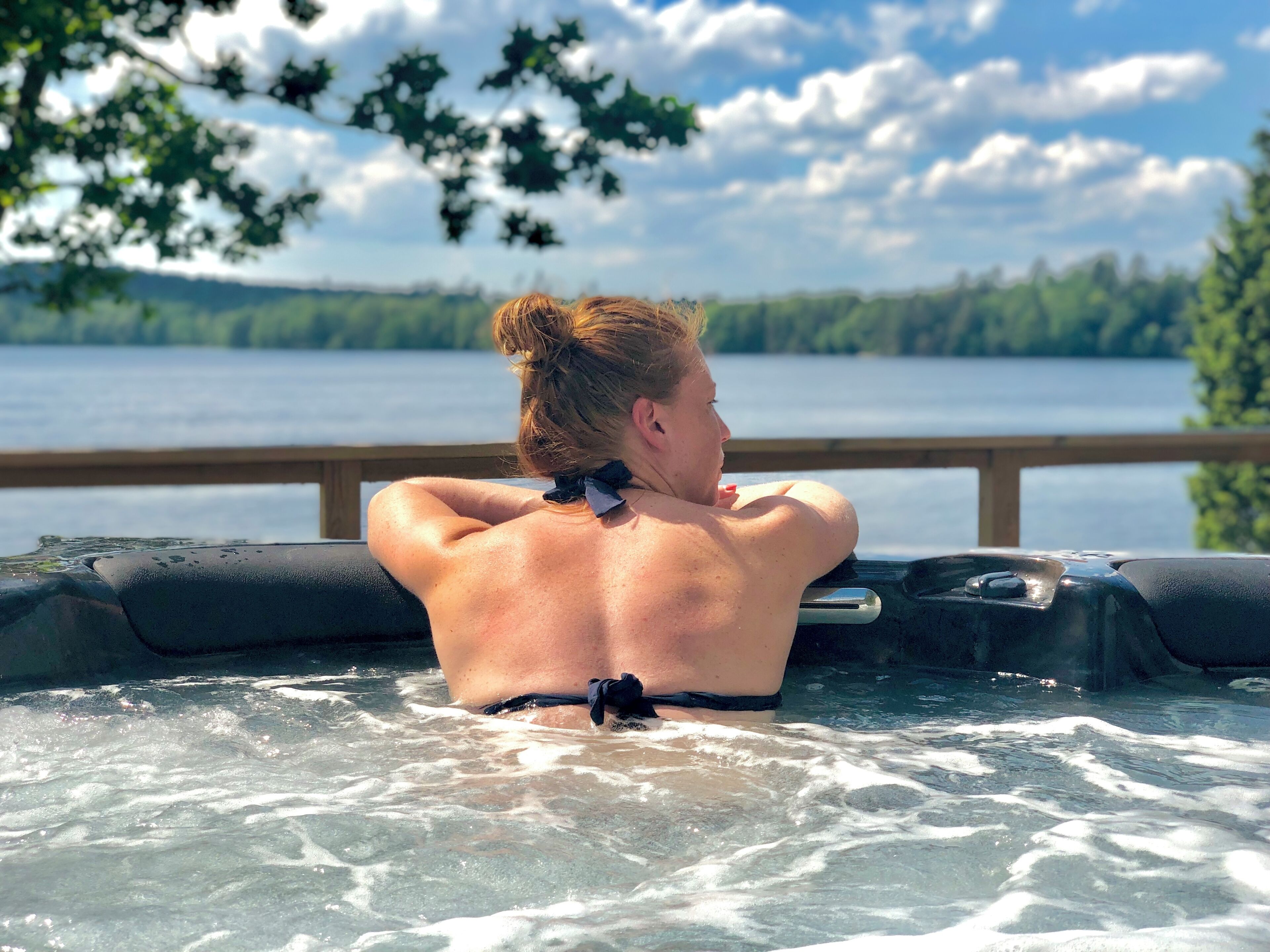 Iemand zit in een jacuzzi met uitzicht op een meer en bos.