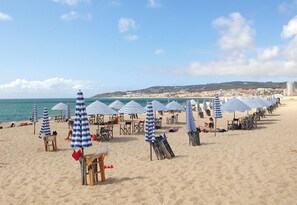 Een strand met rijen blauw-wit gestreepte parasols, strandstoelen en ligbedden.