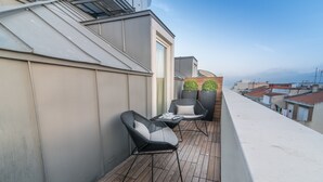 Une terrasse sur le toit avec un plancher en bois, deux fauteuils en osier dotés de coussins et une petite table.
