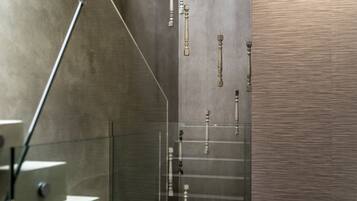 Un baño moderno con separador de vidrio, una escalera de metal y un revestimiento texturizado.