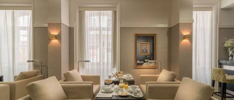 A dining area with a table set for breakfast, surrounded by sofas, and a framed portrait on the wall.