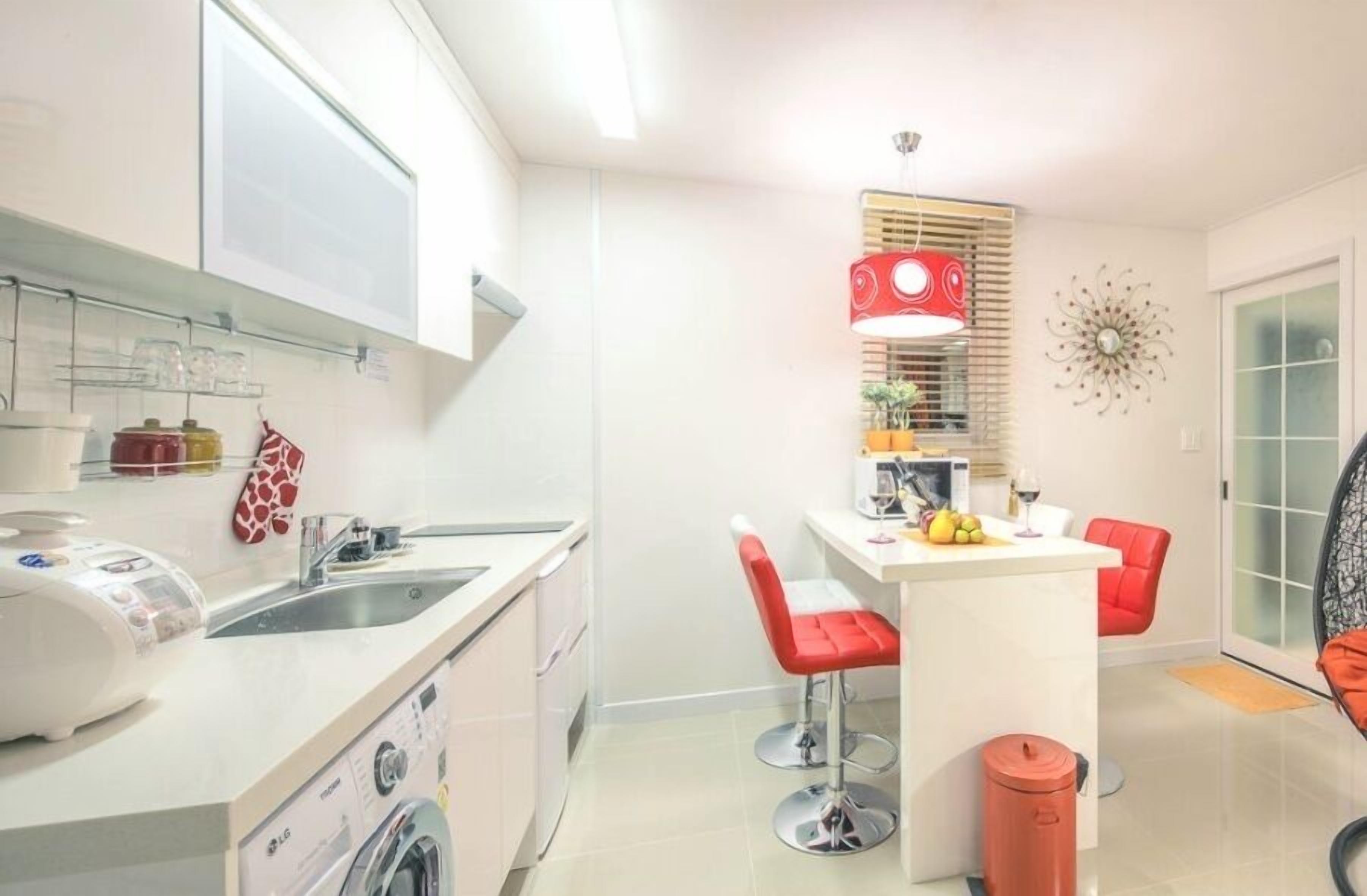Une cuisine compacte équipée d’un lave-linge intégré, d’un évier et d’un petit coin repas avec des chaises rouges.